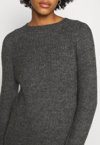 Pull en maille gris foncé avec une texture côtelée, col rond et manches longues, présentant une finition douce et légèrement duveteuse.
