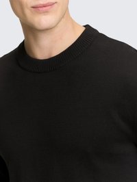 Pull en maille noire avec encolure ronde côtelée. Texture douce, coupe ajustée et tissu lisse sans motifs ni accents visibles.