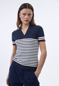 Polo a maniche corte a righe blu navy e bianche, con scollo a V e dettagli rossi sulle maniche, caratterizzato da un design a treccia testurizzato.