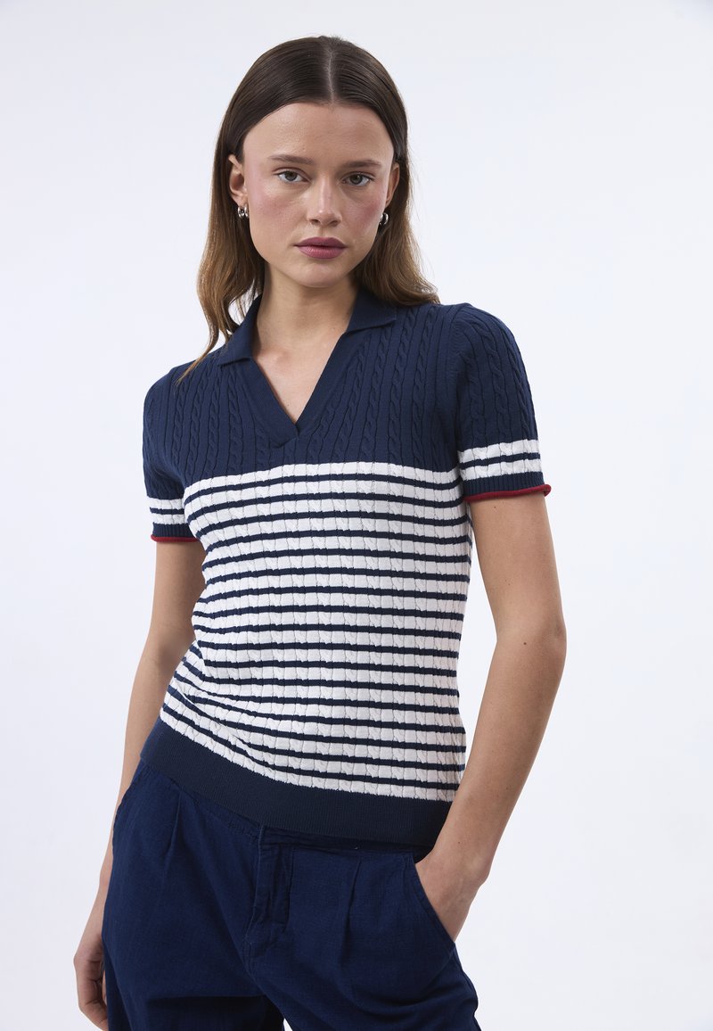 Polo a maniche corte a righe blu navy e bianche, con scollo a V e dettagli rossi sulle maniche, caratterizzato da un design a treccia testurizzato.