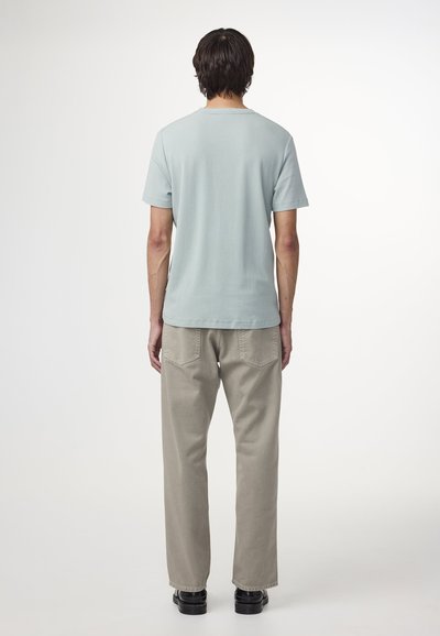 T-shirt azzurro chiaro a maniche corte con collo rotondo, abbinato a pantaloni beige chiaro a gamba dritta e scarpe nere, visto da dietro.