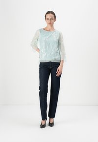 Top azzurro chiaro in chiffon con motivo texturizzato, maniche a tre quarti trasparenti; abbinato a jeans blu scuro e tacchi neri. Design semplice e moderno.
