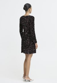 Must mustrilineeritud must kleit pikkade varrukatega, põlvepikkune hem ja lukuga sulgur taga. Hõbedased kontsakingad täiendavad riietust.