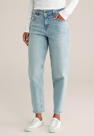 Jeans de tiro alto azul claro con pierna acampanada, grandes bolsillos frontales y un sutil desgastado. Combinados con zapatillas blancas con acentos grises.