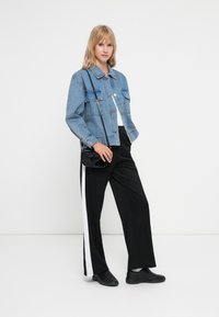 Hele sinine denim-jakk kahe ees oleva taskuga, mustad ja valged spordipüksid ning mustad tossud. Mudel kannab väikest musta õlakotti.