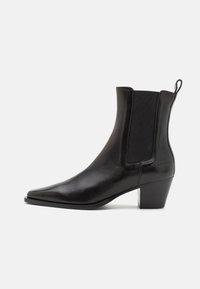 Botín de cuero negro con punta puntiaguda, paneles laterales elásticos y un tacón bajo apilado, con una lengüeta para facilitar su uso.