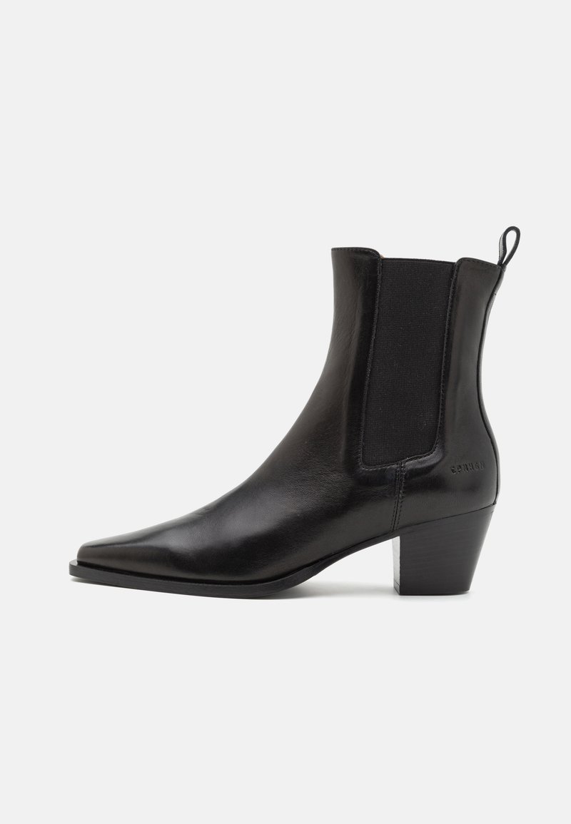 Botín de cuero negro con punta puntiaguda, paneles laterales elásticos y un tacón bajo apilado, con una lengüeta para facilitar su uso.