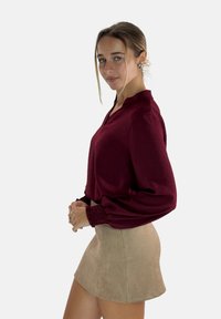 Bordeaux lange mouwen blouse met een kraag en geplooide manchetten, gecombineerd met een beige suède minirok. Glad, gewatteerd materiaal.