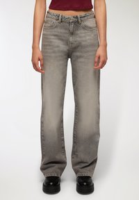 Szare dżinsy z wysokim stanem, prostym krojem nogawki i delikatnym wyblaknięciem. Posiadają pięć kieszeni oraz zapięcie na guzik.