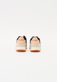 Schwarze und beigen Sport Schuhe mit einem strukturierten Obermaterial, gepolstertem Fersenbereich in Orange und Gummisohle. Mit "CLAE" Branding an der Ferse.