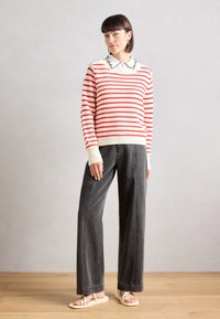 Red and white striped knit sweater with a ruffled white collar, paired with gray wide-leg pants and beige sandals on a wooden floor.