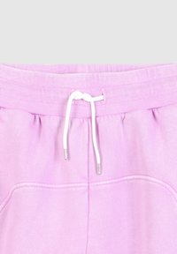 Lichtpaarse trainingsbroek met geribbelde tailleband en witte trekkoord dat in een knoop in het midden is geknoopt.