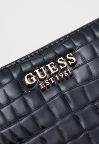 Clutch nera in ecopelle con texture a pelle di coccodrillo, caratterizzata da un logo dorato "GUESS EST. 1981" in bella mostra.