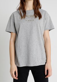 Camiseta de algodón gris con un corte relajado y mangas cortas, con un diseño de logo simple en dorado en la zona del pecho.