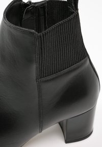 Bottine noire en cuir avec un insert en tissu à côtes, un talon carré et une finition lisse, présentant des coutures contrastées le long de la couture latérale.