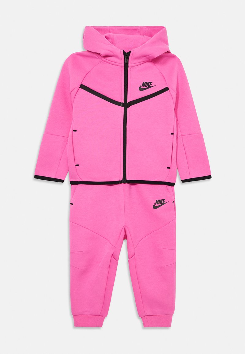 Różowy dres Nike z kapturem na zamek błyskawiczny i czarnymi akcentami, oraz dopasowane spodnie z detalami logo na klatce piersiowej i nogawce.