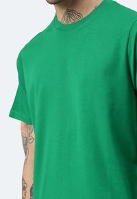 T-shirt in cotone verde con maniche corte. Design a girocollo; texture liscia; presenta cuciture visibili e una vestibilità rilassata.