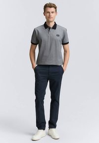 Halli lühikeste varrukatega polo-särk musta krae ja varrukakääristega, tumelilla pükstega ja valgete tennistega, neutraalse taustaga.