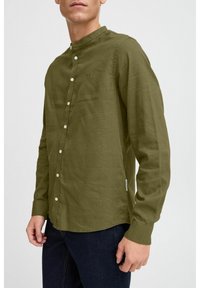 Olivengrünes Langarmshirt aus leichtem Stoff, mit Stehkragen, Knopfverschluss und seitlichem Etikettendetail.