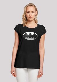 Svart t-skjorte med korte ermer laget av bomull, med et hvitt Batman-logo med prikkemønster foran. Glatt tekstur, avslappet passform.