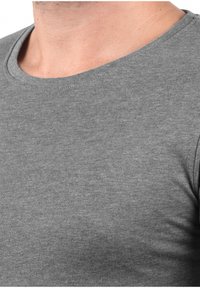 Camiseta de algodón gris con cuello redondo. La tela parece suave con una superficie ligeramente texturizada, con mangas cortas.