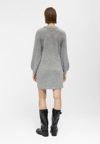 Abito maglione grigio lavorato a maglia con maniche a palloncino lunghe, abbinato a stivali neri in pelle al ginocchio con cinture e fibbie regolabili.