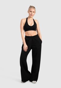 Sort sportsbh og brede sweatpants. Stoffet er blødt med en glat tekstur. Har en elastisk talje og kontrasterende syninger.