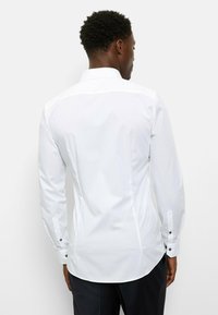 Weißes Langarmhemd mit taillierter Passform, klassischem Kragen und schwarzen Knopf-Akzenten an den Manschetten. Glattes, leichtes Material.