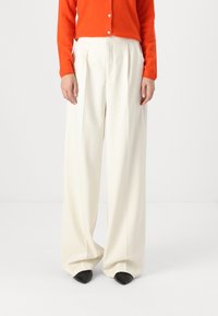 Wide-leg trousers in soft, white fabric, featuring pleats and a loose fit. Paired with an orange cardigan and black pointed-toe heels.