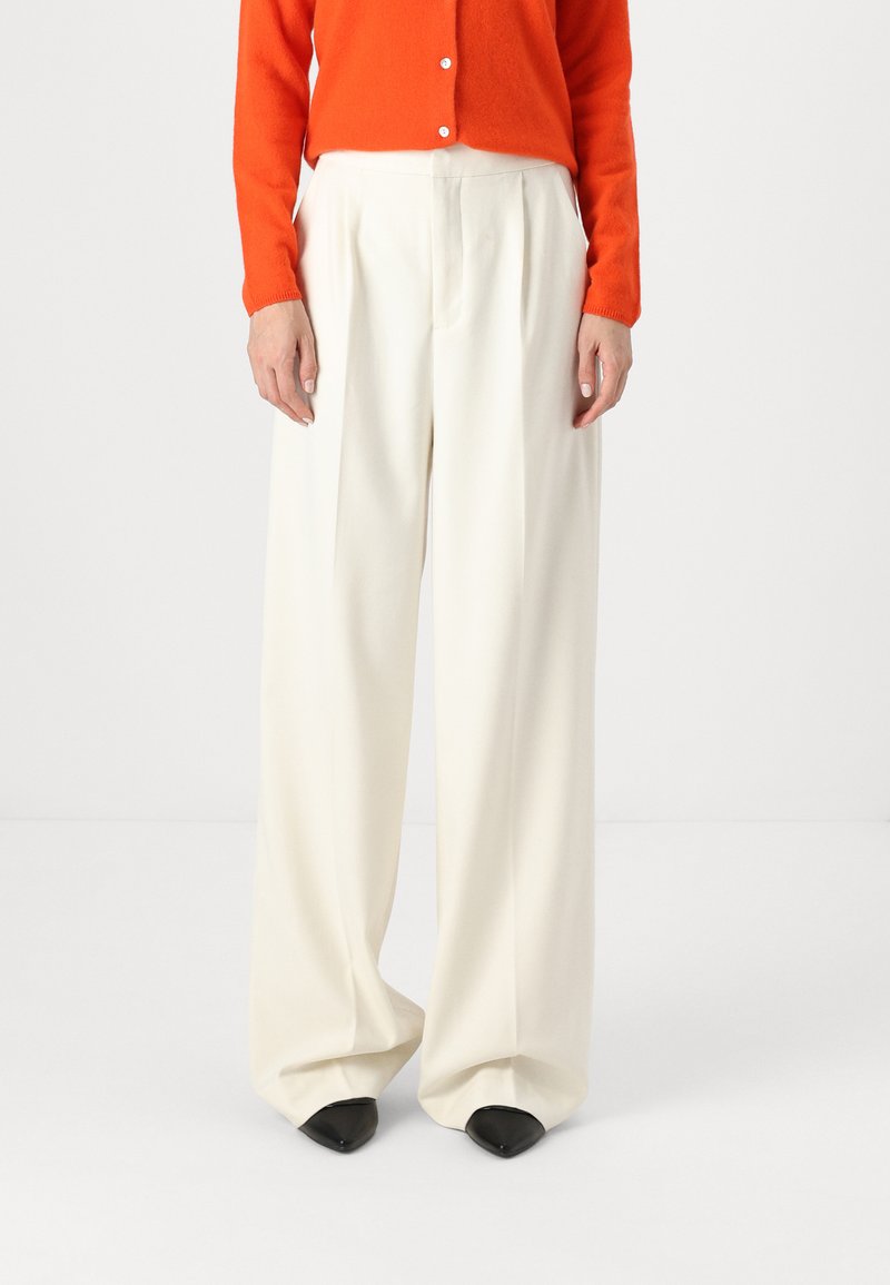 Wide-leg trousers in soft, white fabric, featuring pleats and a loose fit. Paired with an orange cardigan and black pointed-toe heels.