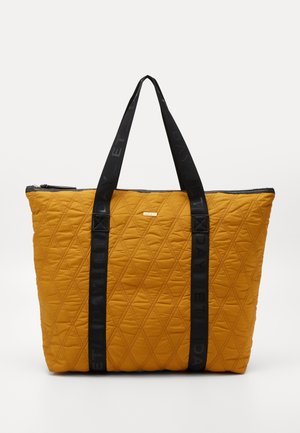 Quiltet sennepsgul tote-taske med sorte håndtag med gentaget tekst, lynlås lukning og en lille frontlogo etiket.