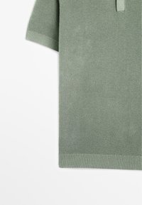 Polo a maniche corte in tessuto testurizzato di color verde chiaro, con motivo a maglia, colletto e polsini a costine, che mette in evidenza una vestibilità comoda.