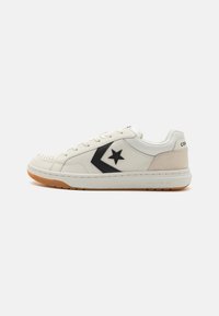 White leather sneakers with black star logo and accent, featuring a gum rubber sole and subtle suede detail on the heel. Classic design.