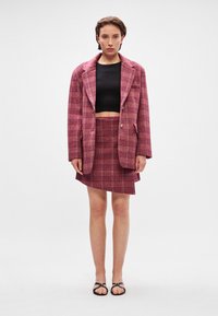 Rozā kvadrātveida žakete ar iekļautām atloks, apvienota ar melnu īsu topu un atbilstošu kvadrātveida mini svārku. Šī komplekta akcenti ir vienkārši melni sandales.