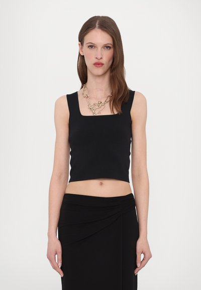 Top noir court avec un col carré, fabriqué dans un tissu lisse ; associé à une jupe noire avec un design torsadé. Accent collier en or.