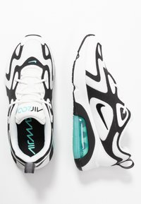 Vita och svarta träningsskor med en strukturerad tygövre, vågig design och en genomskinlig turkos luftenhet i sulan.