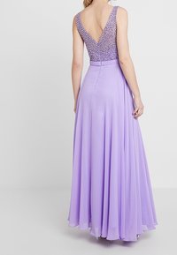 Lilaruusuinen iltamekko V-mallisella selkäosalla, jossa on paljettimekko ja hulmuava helma. Kangas on sileä ja kevyt, mikä korostaa liikkuvuutta.