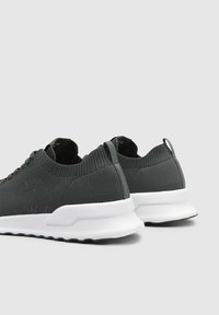 Zapatillas de tejido gris con una parte superior texturizada, suela intermedia blanca y lengüeta trasera. Presenta una puntera redondeada y suela de goma flexible.
