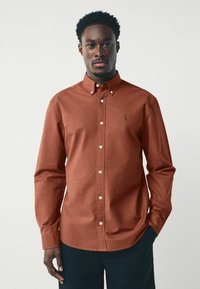 Camicia button-up marrone in cotone, con colletto, maniche lunghe, pattina frontale con bottoni bianchi e un piccolo logo sul petto.