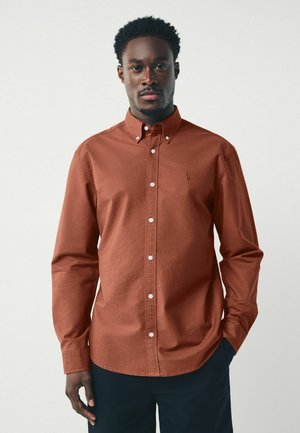 Brown button-up shirt made of cotton, featuring a collared neckline, long sleeves, front placket with white buttons, and a small logo on the chest.