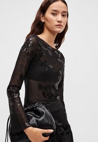 Top preto de manga comprida com padrão floral transparente e lantejoulas. Tecido texturizado com uma silhueta ajustada, combinado com uma bolsa preta com cordão.