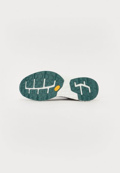 Såle til en joggesko med grønn gummisåle og hvit mellomsåle, med en liten oransje Vibram-logo i midten av sålen.