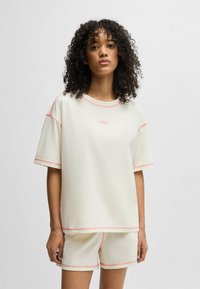 Ljus krämfärgad träningsset som består av en kortärmad topp och shorts, accentuerad med rosa sömmar. Mjukt tyg, avslappnad passform, minimalistisk branding.