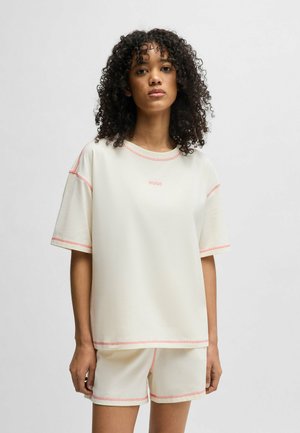Light cream athletic set featuring a short-sleeve top and shorts, accented with pink stitching. Soft fabric, relaxed fit, minimal branding.