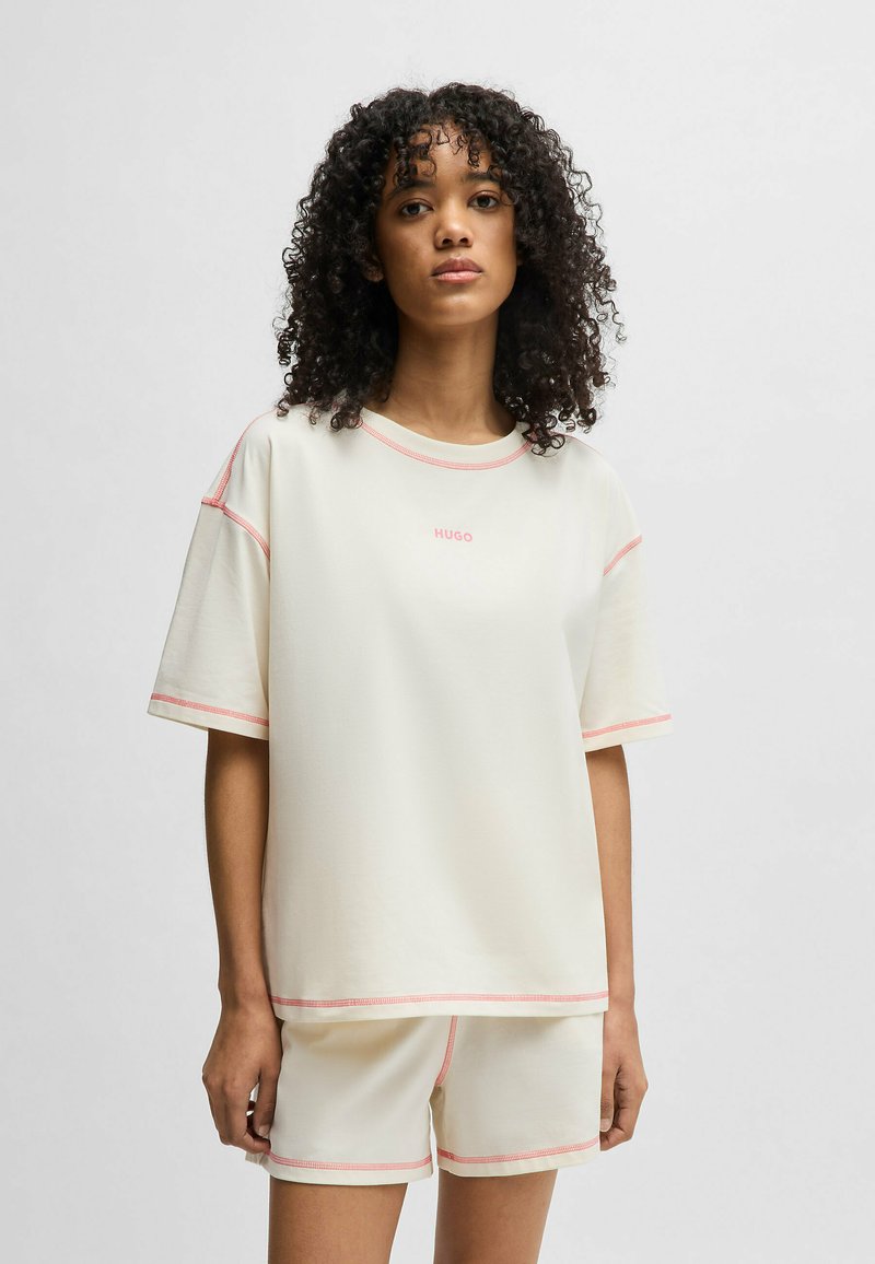 Ljus krämfärgad träningsset som består av en kortärmad topp och shorts, accentuerad med rosa sömmar. Mjukt tyg, avslappnad passform, minimalistisk branding.