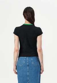 Black short-sleeve t-shirt with a green collar, fitted design. Paired with a blue denim skirt featuring patch pockets on the back.