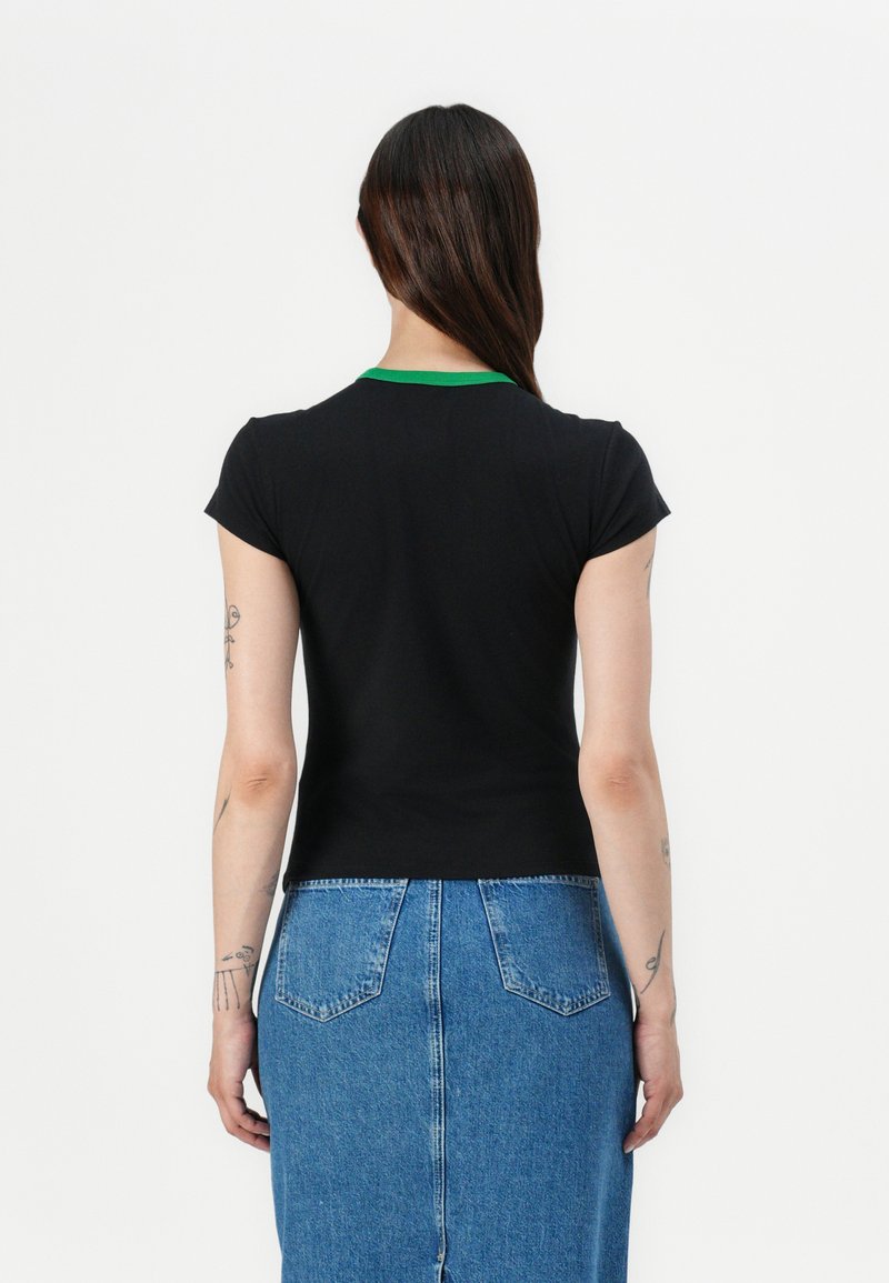 Schwarzes T-Shirt mit kurzen Ärmeln und grünem Kragen, taillierte Passform. Kombiniert mit einem blauen Denim-Rock mit aufgesetzten Taschen auf der Rückseite.