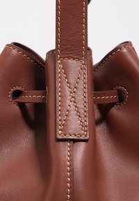 Pruunist nahast koti nurga lähivaade, kus on näha detailne beež õmblus ja käepide, mis on läbi metallist silmade läbi keeratud.