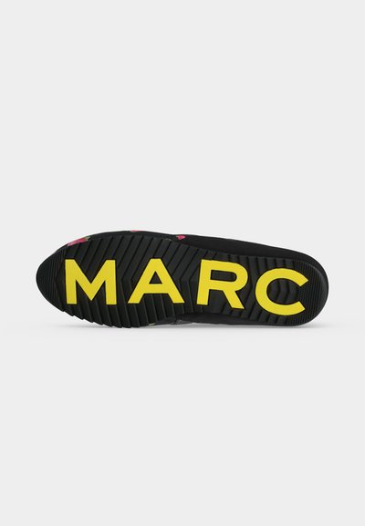 Semelle de chaussure noire avec des rainures profondes et de grandes lettres jaunes épelant "MARC" sur le dessous.