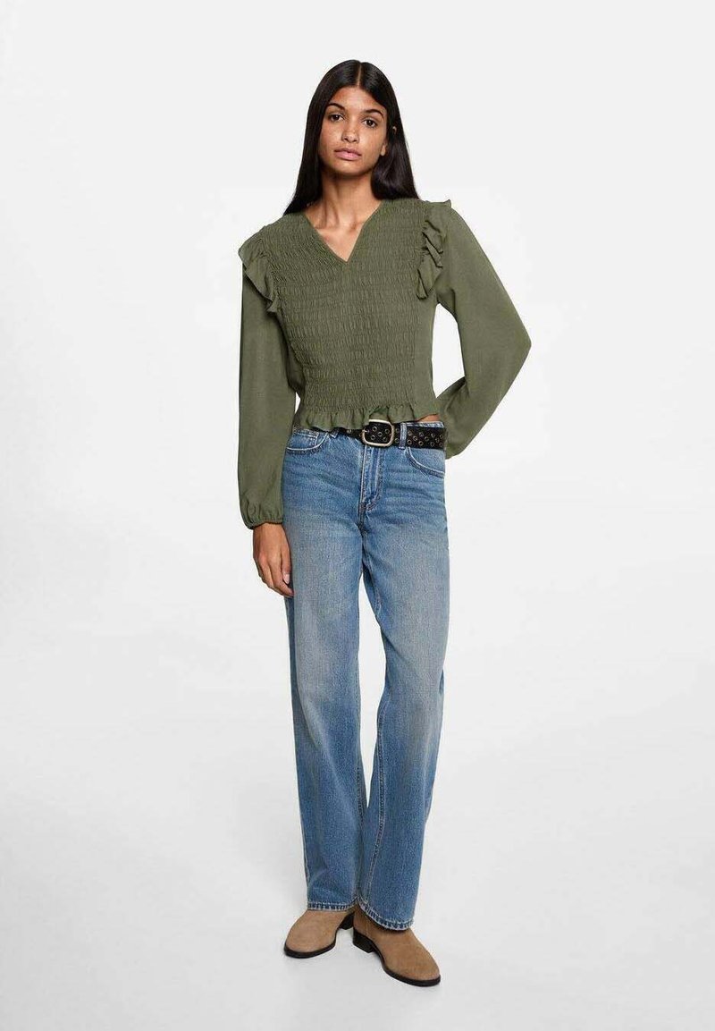 Olivgrön, smockad bomullblus med V-hals, volangärmar och kortad nederkant, parat med ljusblå raka jeans och beige ankelskor.